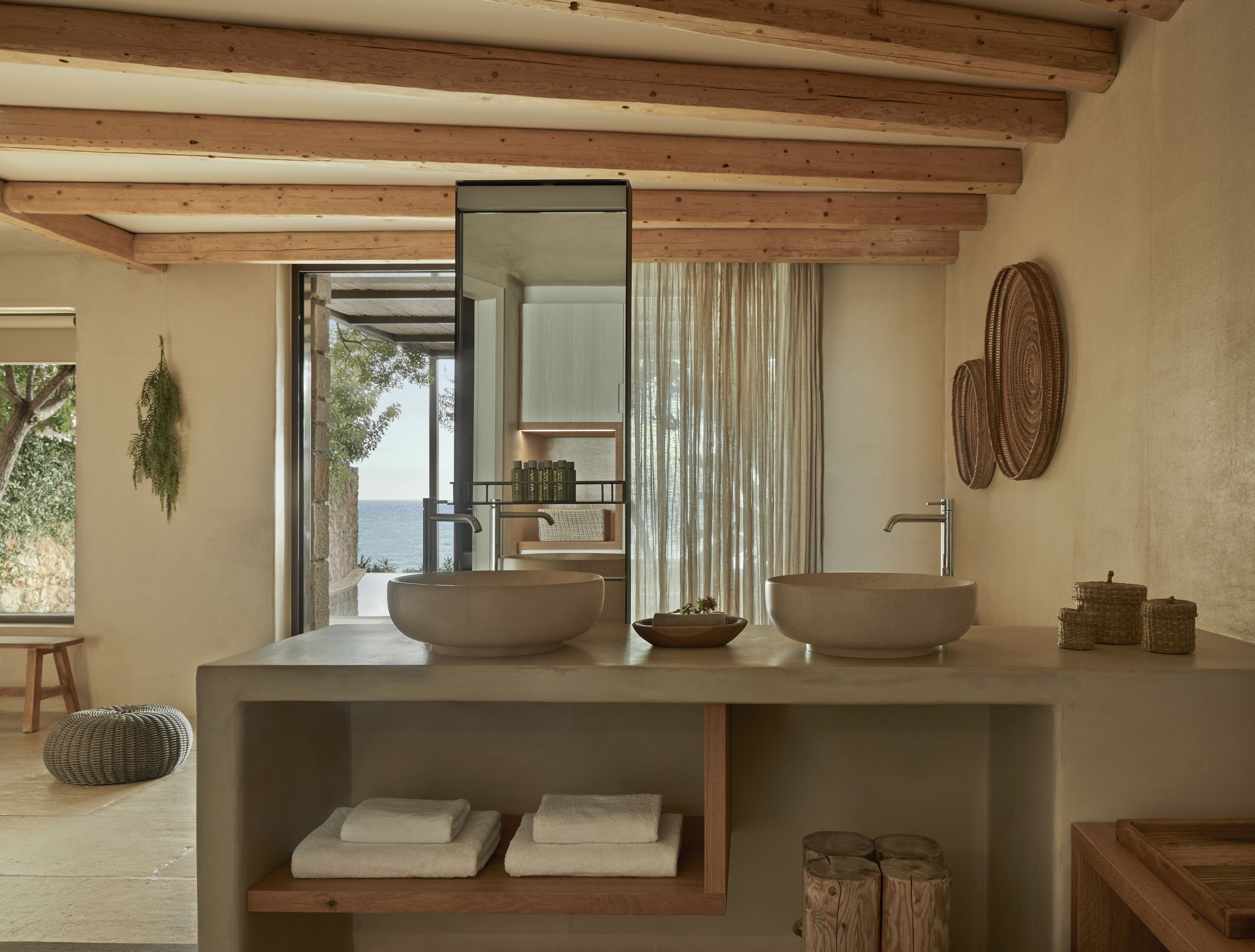 Un baño moderno con un espejo grande, dos lavamanos y vista al mar.