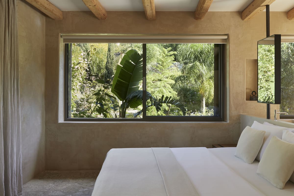 A bedroom with a large window, a bed with white linens, and a wooden ceiling.