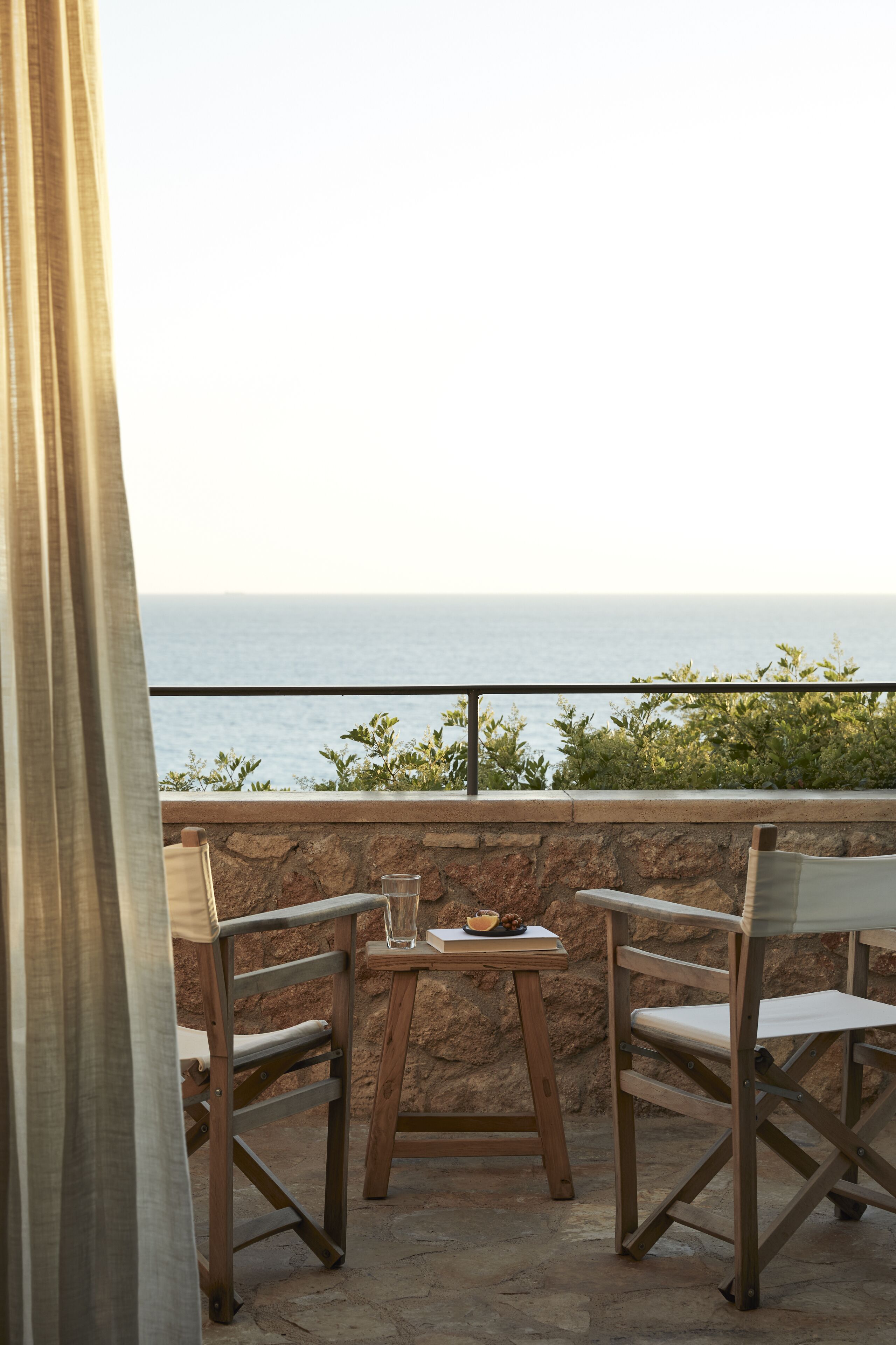 A balcony with two wooden chairs and a table, overlooking the sea.