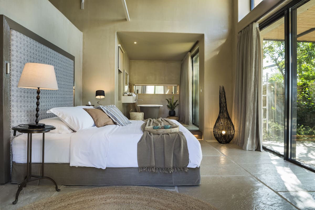 A modern bedroom with a large bed, bedside lamps, a bedside table, and a view of the bathroom.