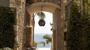 Un arc en pierre menant à un balcon d’où l’on peut admirer la mer, un luminaire suspendu et un fauteuil en osier.