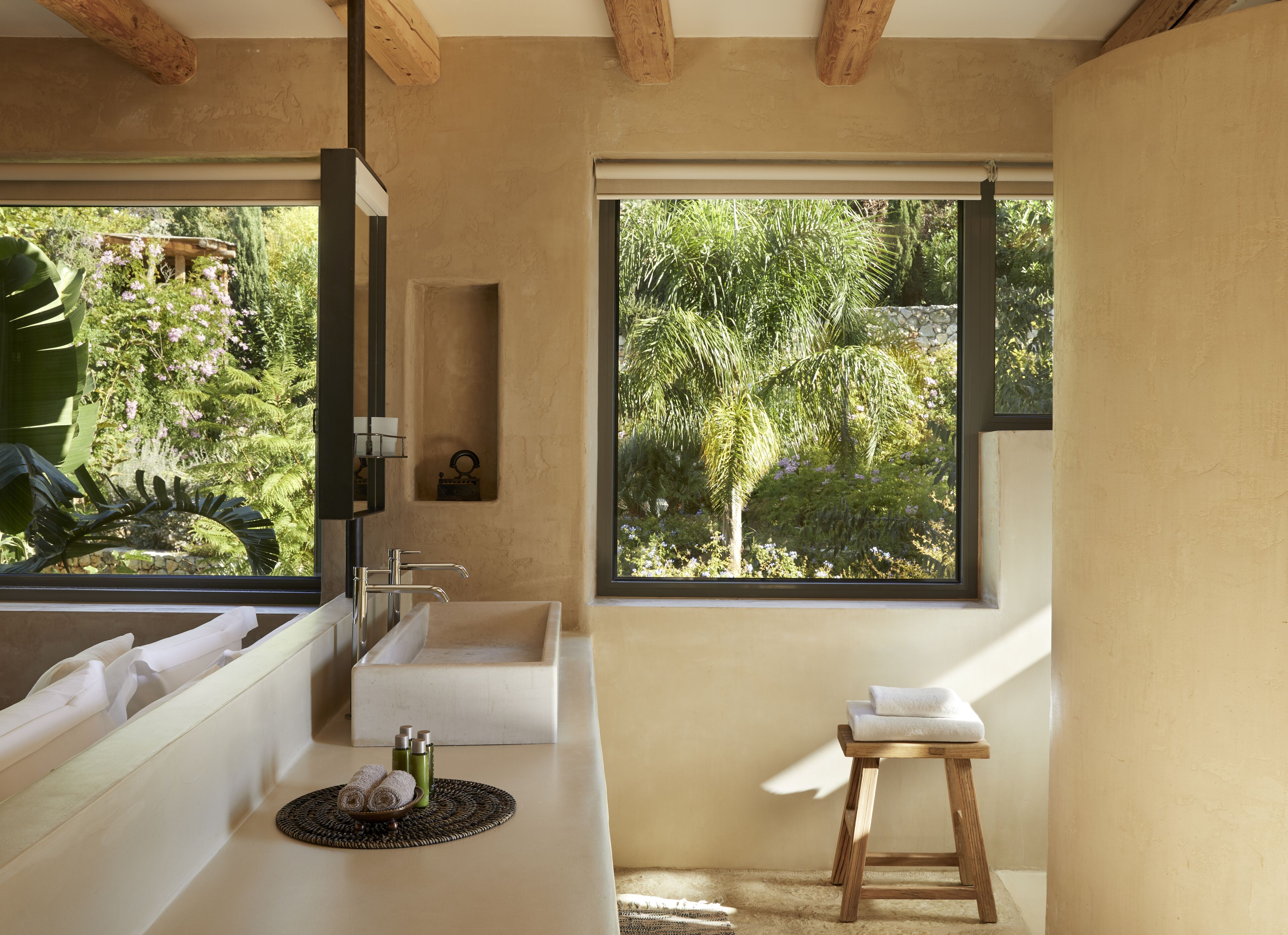 Un baño moderno con un ventanal grande, un lavabo y un taburete de madera.