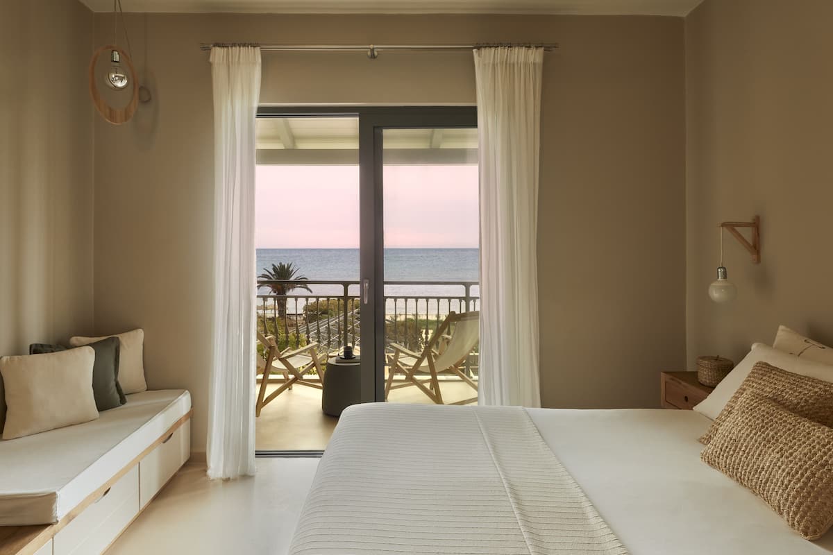 A bedroom with a large bed, a balcony with a view of the sea, and a seating area with a view of the sea.