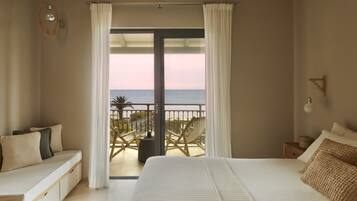 A bedroom with a large bed, a balcony with a view of the sea, and a seating area with a view of the sea.