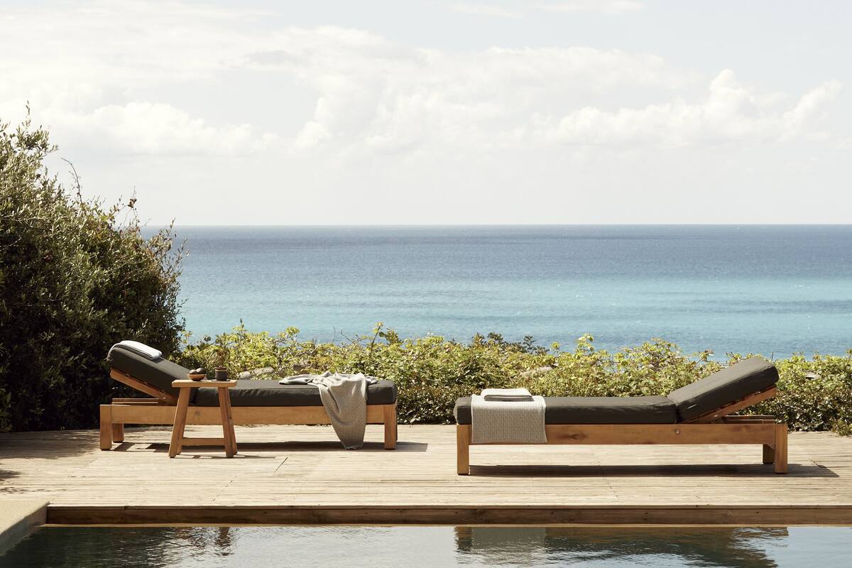 A poolside area with two lounge chairs and a wooden deck overlooking the ocean.