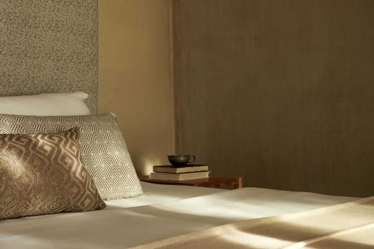 A neatly made bed with patterned pillows, a stack of books, and a small table with a cup.