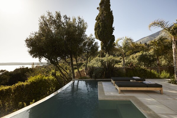 A pool with lounge chairs, surrounded by trees and a view of the water.