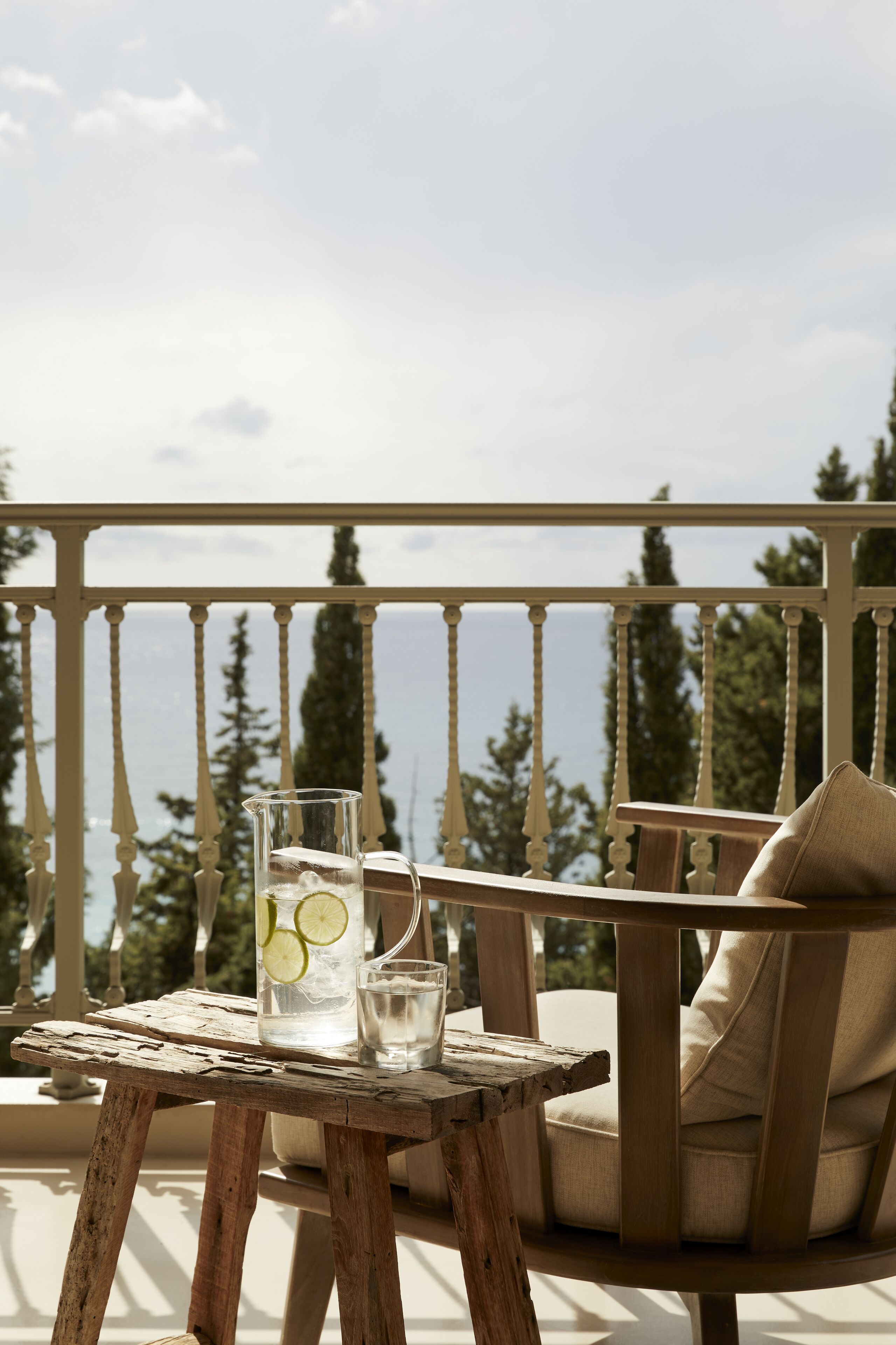 A wooden table with a pitcher and glasses on a balcony overlooking a scenic view.