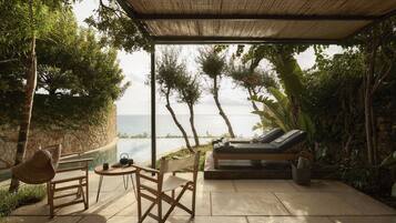 Un espace extérieur aménagé avec une terrasse couverte, offrant une vue sur la mer, doté de mobilier en bois et entouré d’une végétation luxuriante.