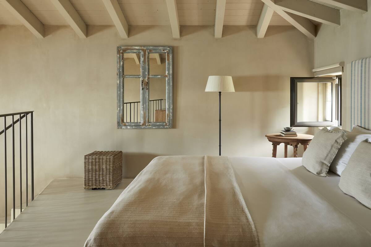 A bedroom with a bed, a lamp, a mirror, and a window.