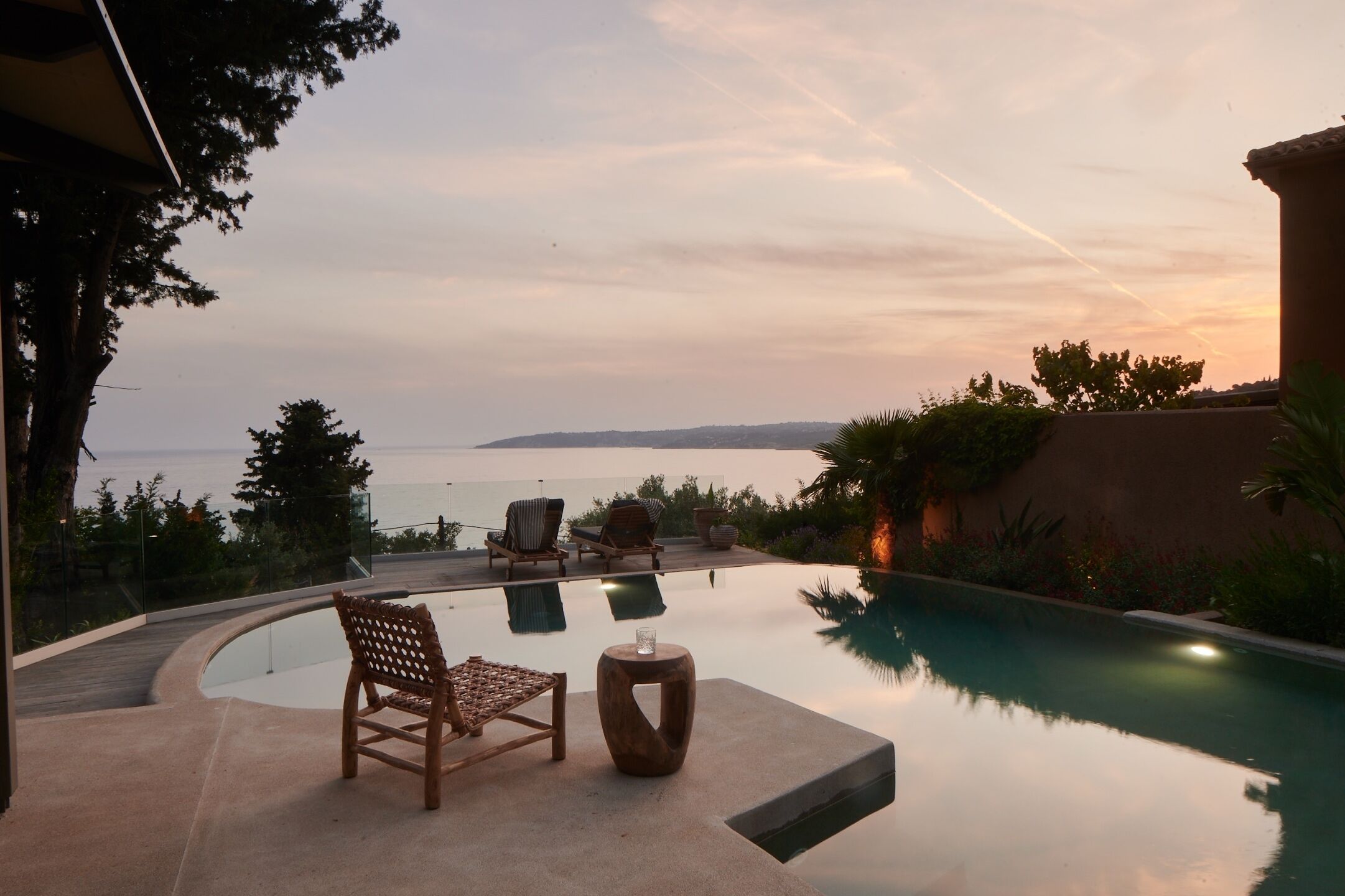 A poolside area with lounge chairs and a small table, overlooking a body of water and distant hills.