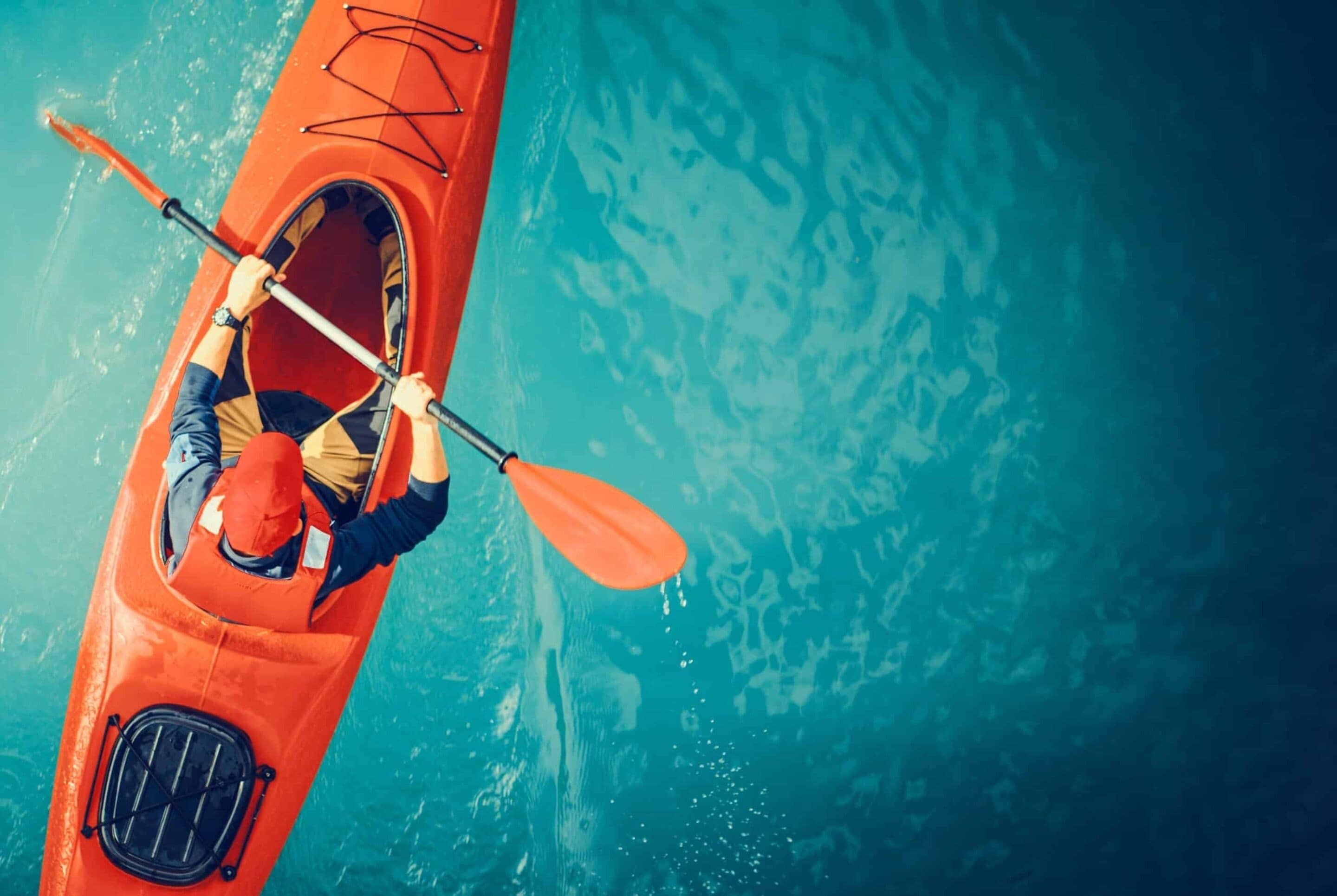 Una persona en un kayak rojo con un remo, navegando por aguas azul cristalino.