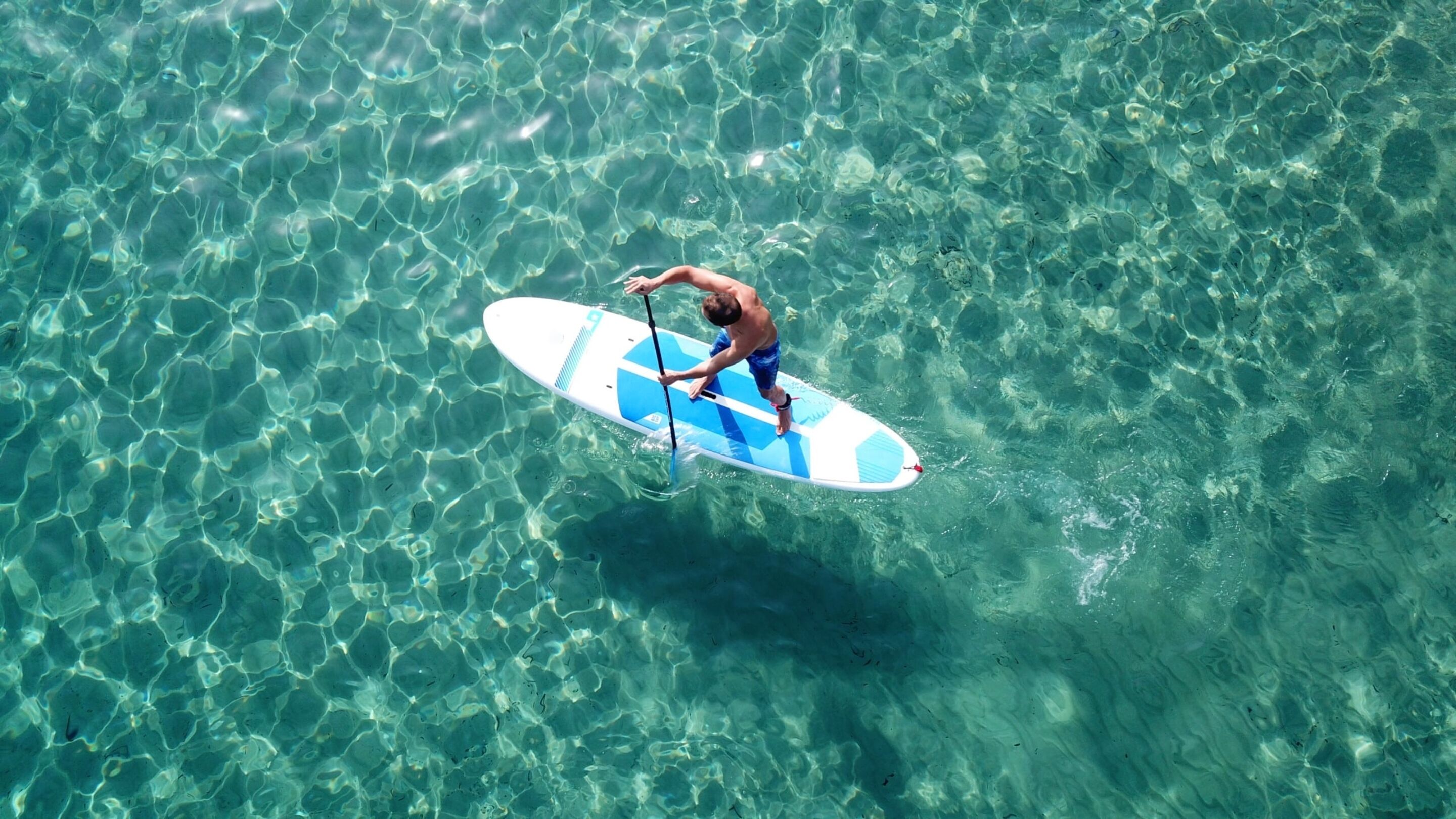 A person standing on a paddleboard in clear water.