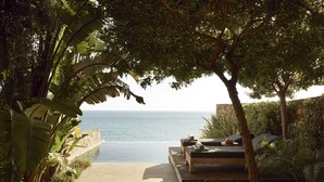 Un espace extérieur isolé, aménagé pour s’asseoir, avec vue sur la mer et entouré d’une végétation luxuriante.