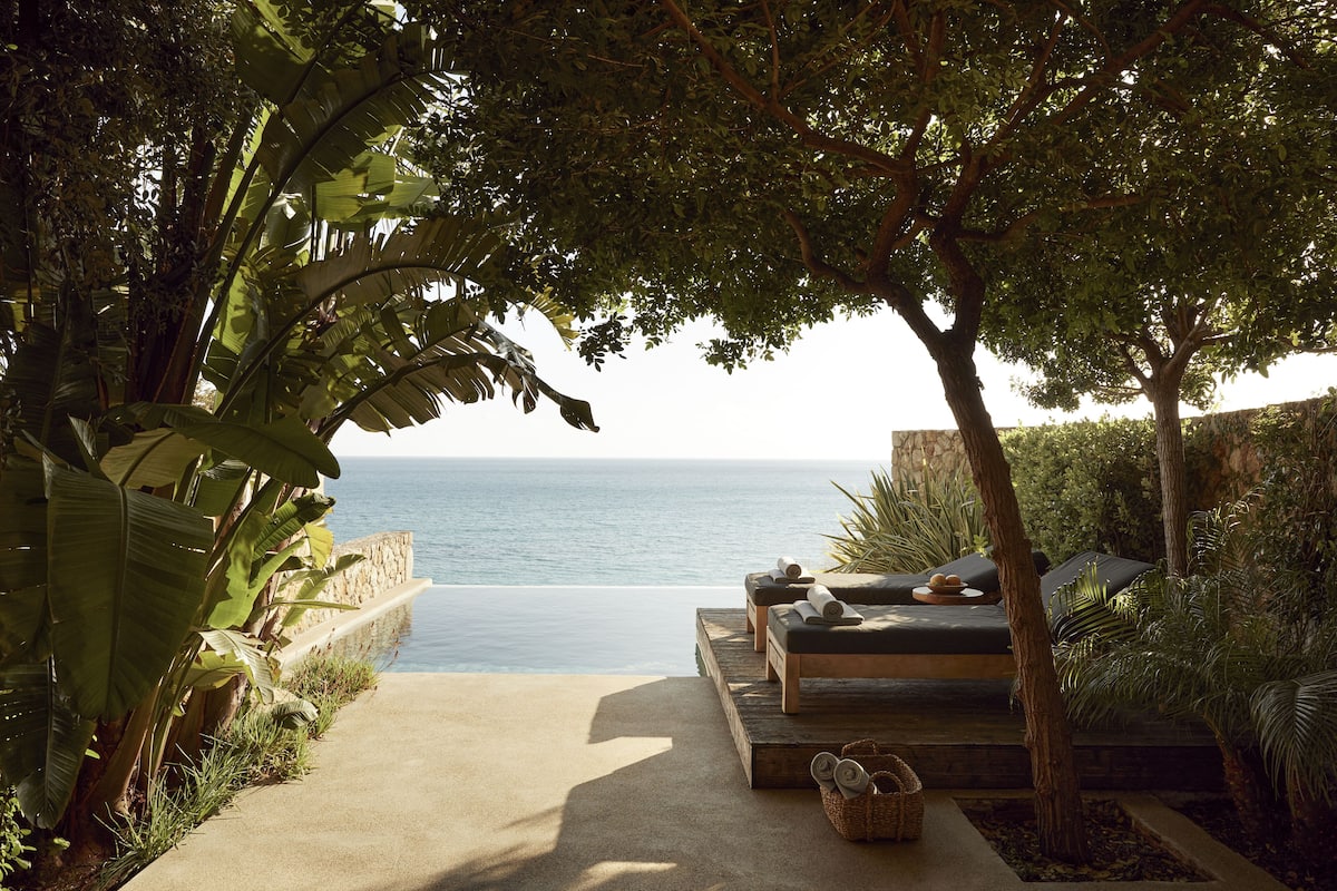 A secluded outdoor seating area with a view of the sea, surrounded by lush greenery.