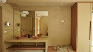 A modern bathroom with a large mirror, two copper sinks, and a wooden bench with a towel.