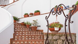 Una escalera con baldosas de terracota, plantas en macetas y barandilla de hierro forjado.