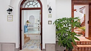 Entrada de hotel con puerta de vidrio, una planta en maceta y suelo de baldosas.