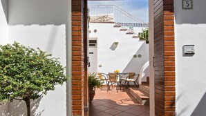 Un estrecho sendero que lleva a un patio con una mesa, sillas, una escalera y un pequeño árbol.