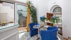 Una habitación pequeña y luminosa con un ventanal de vidrio que da a un balcón, una mesita con una silla y una planta en maceta.
