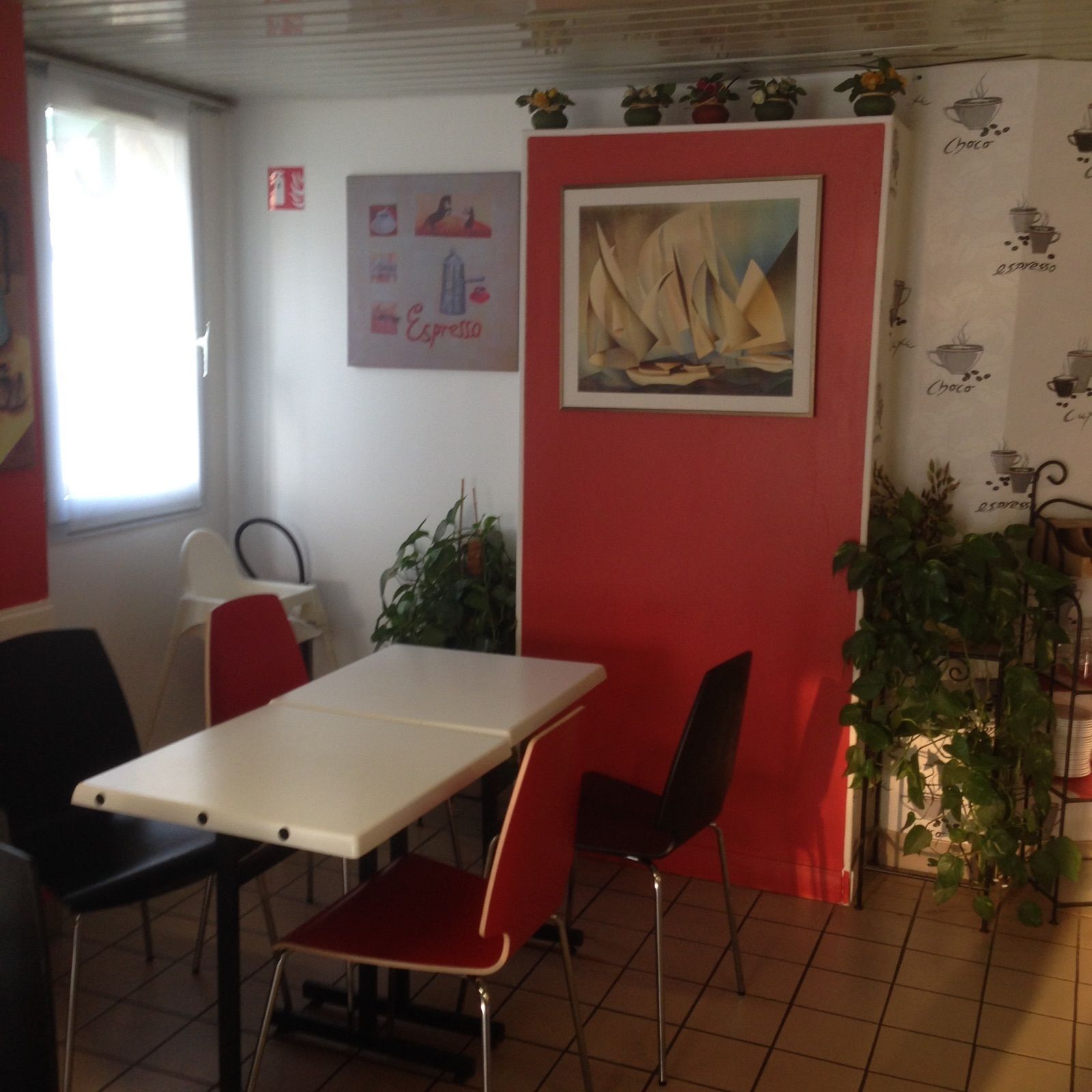 A dining area with a white table and red chairs, a painting on the wall, and a window with curtains.