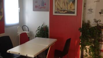 A dining area with a white table and red chairs, a painting on the wall, and a window with curtains.