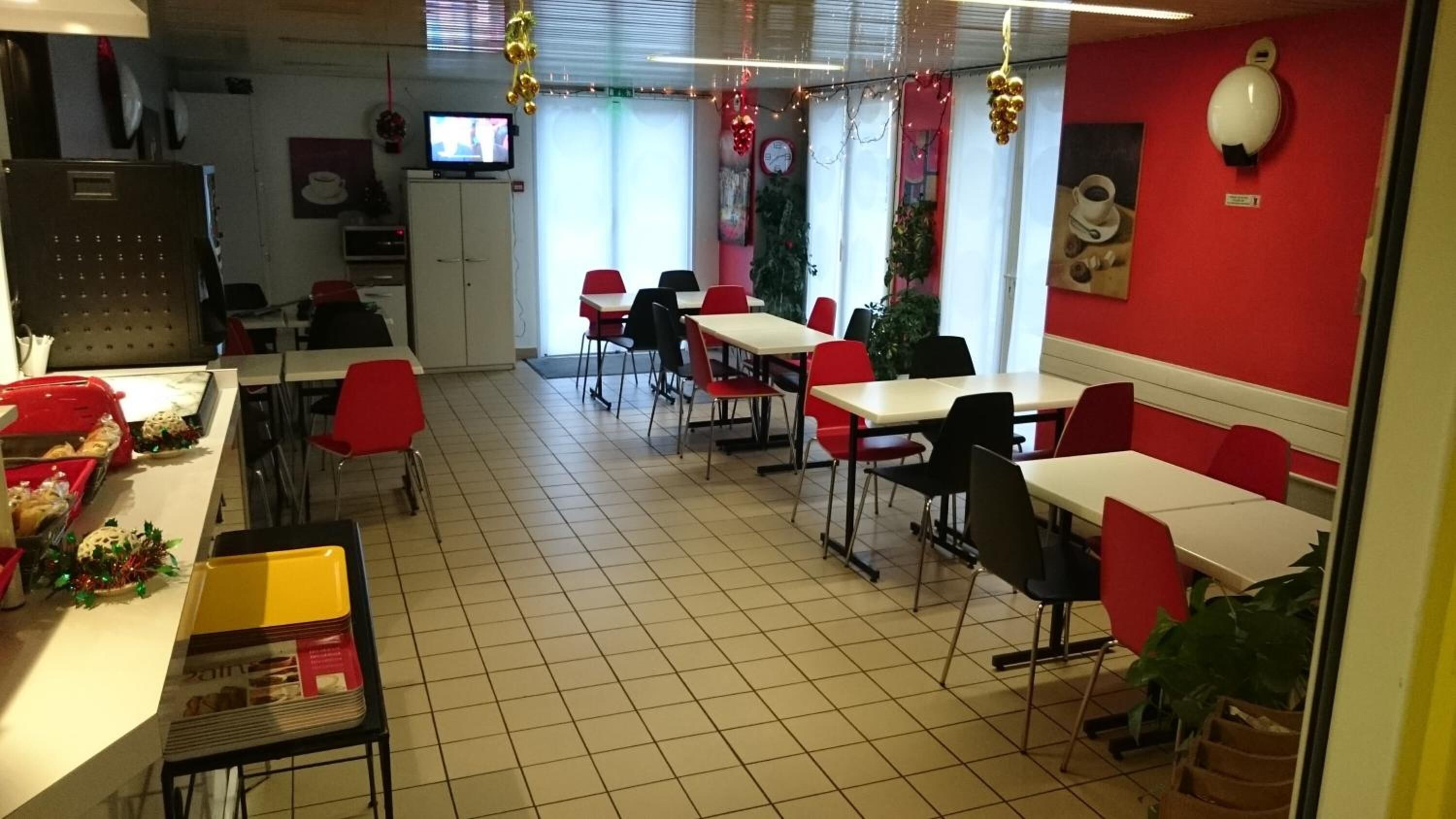 Un coin repas avec des chaises rouges et noires, des tables blanches et un téléviseur posé sur un meuble.