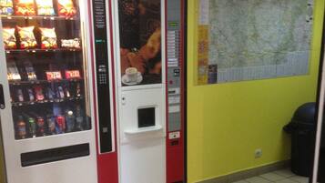 Una máquina expendedora con aperitivos y bebidas, un mapa en la pared y un cubo de basura.