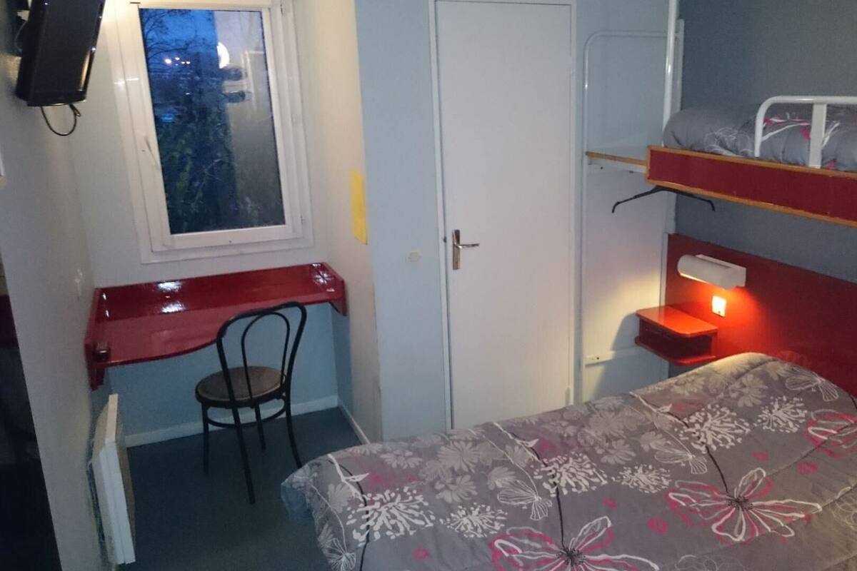 A small room with a bunk bed, a desk with a chair, a window, and a door.
