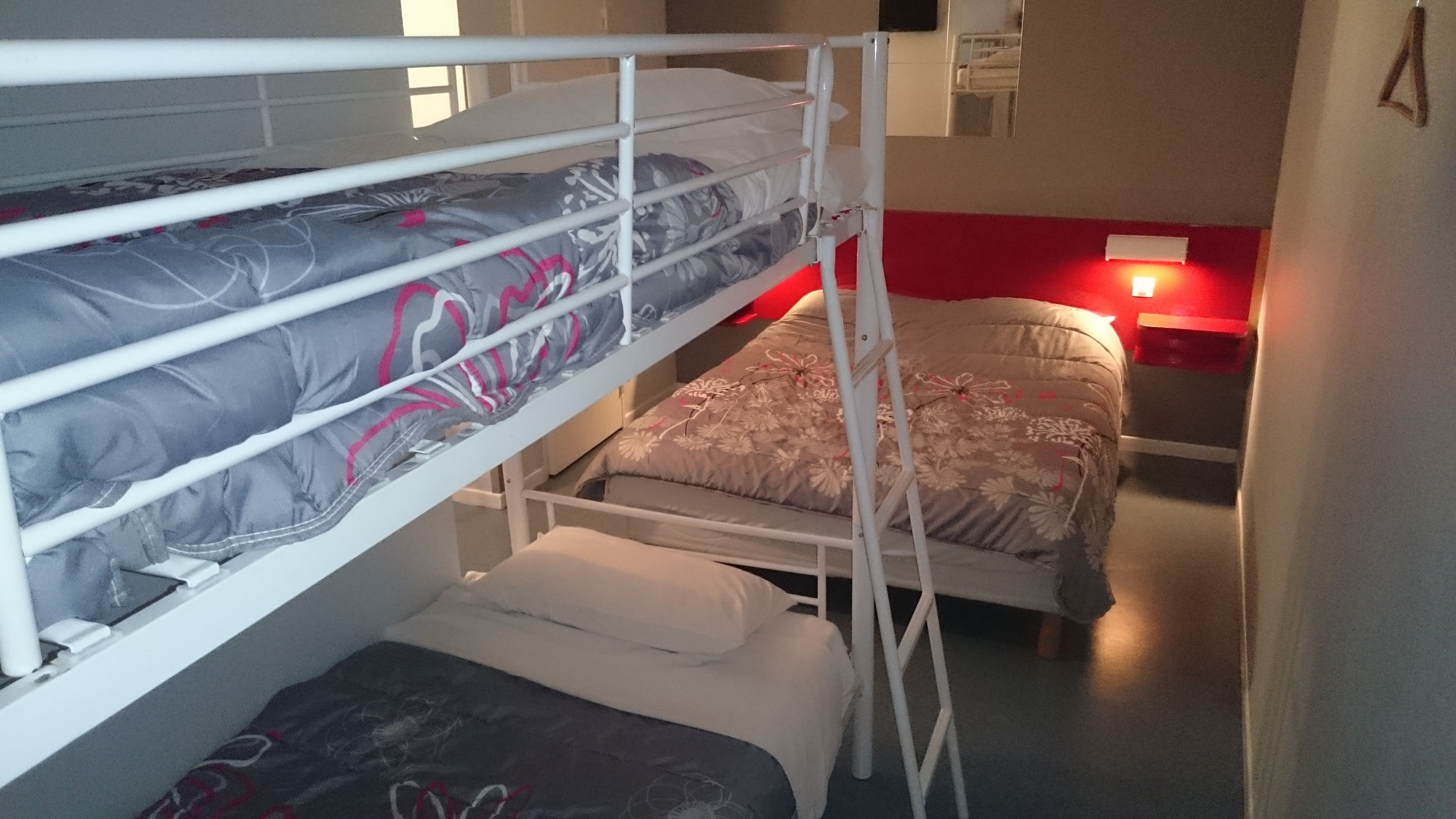 Ein Schlafraum mit Etagenbett, roter Wand und einem kleinen Nachttisch.