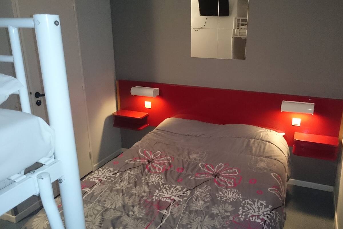 A small, compact bedroom with a single bed, two bedside tables, and a wall-mounted TV.