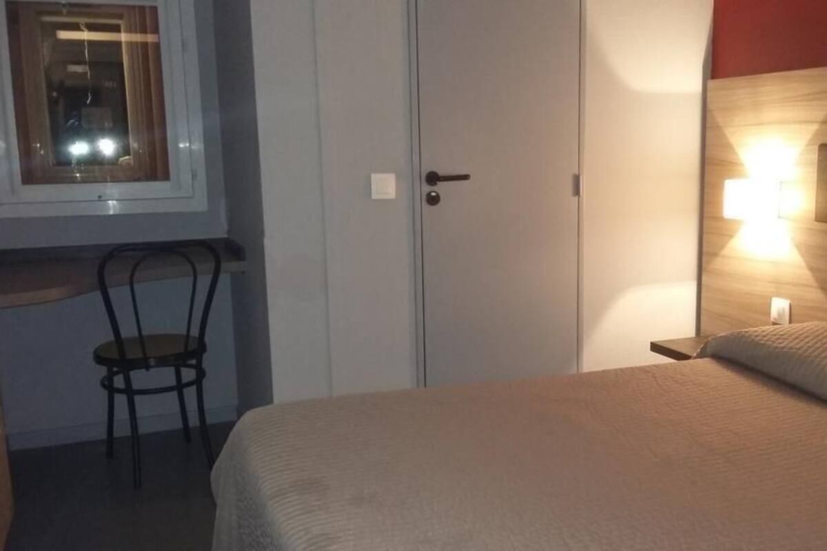 A bedroom with a bed, a chair, a desk, and a window.