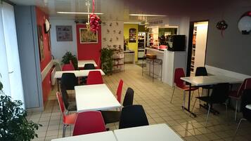 A restaurant interior with red and white tables and chairs, a counter area, and a tiled floor.