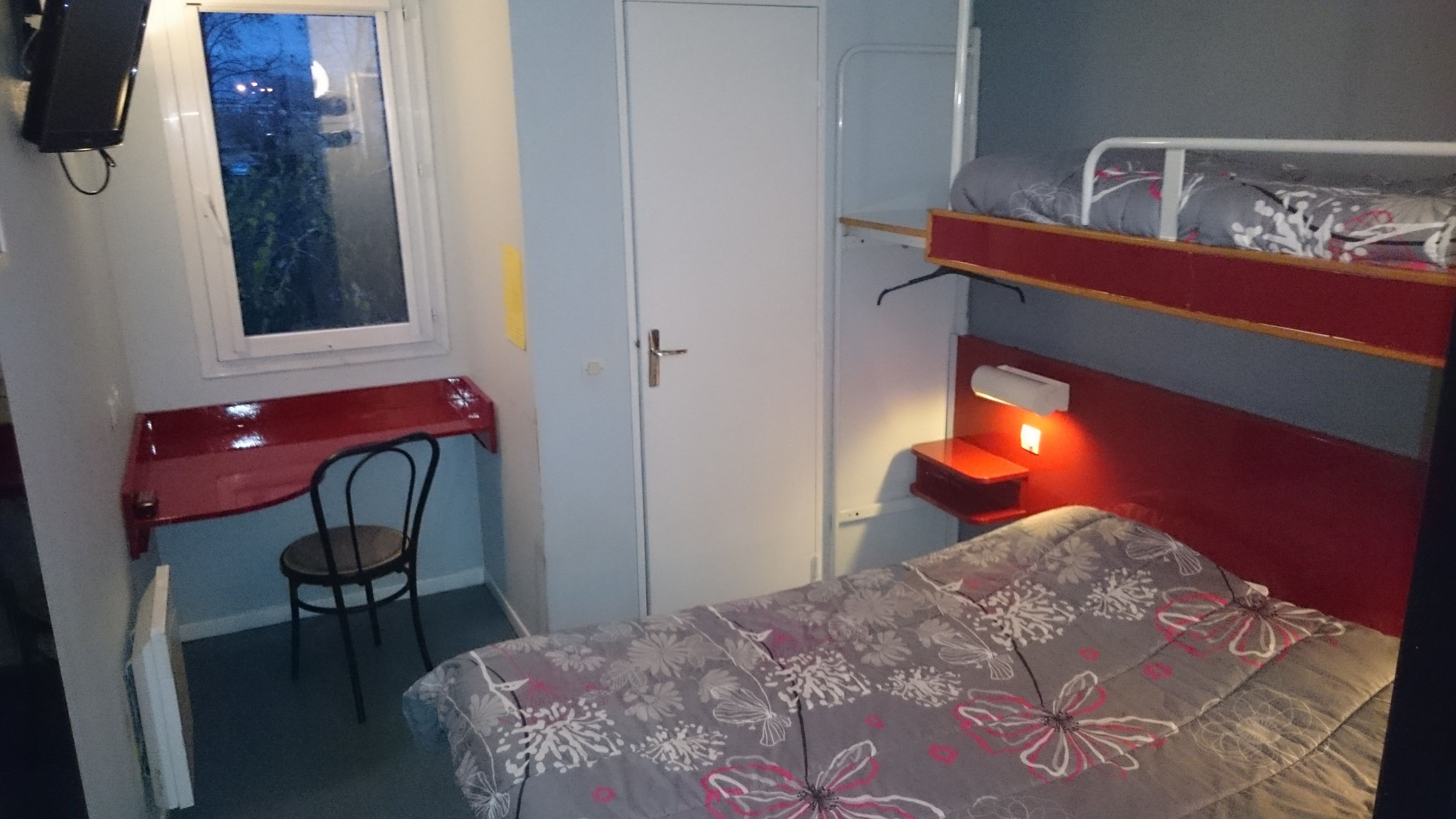 Una habitación compacta con una litera, un escritorio con silla, una ventana y una mesita de noche con lámpara.