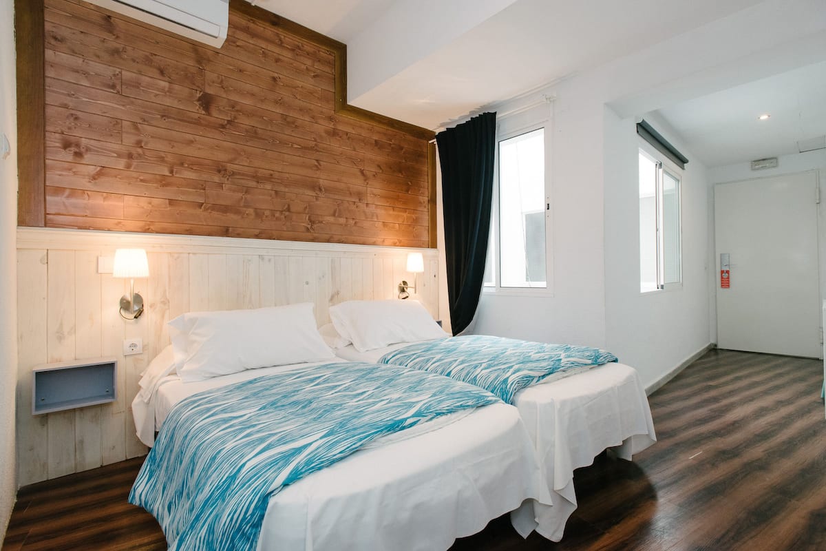 A room with two beds, wooden paneling on the walls, a white ceiling, and a door with a window.