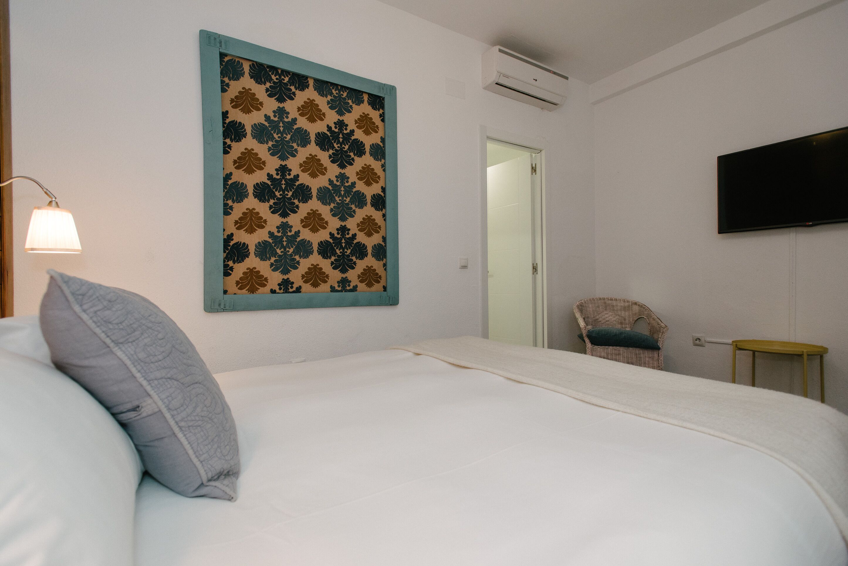 A bedroom with a bed, a wall-mounted TV, a chair, and a small table.