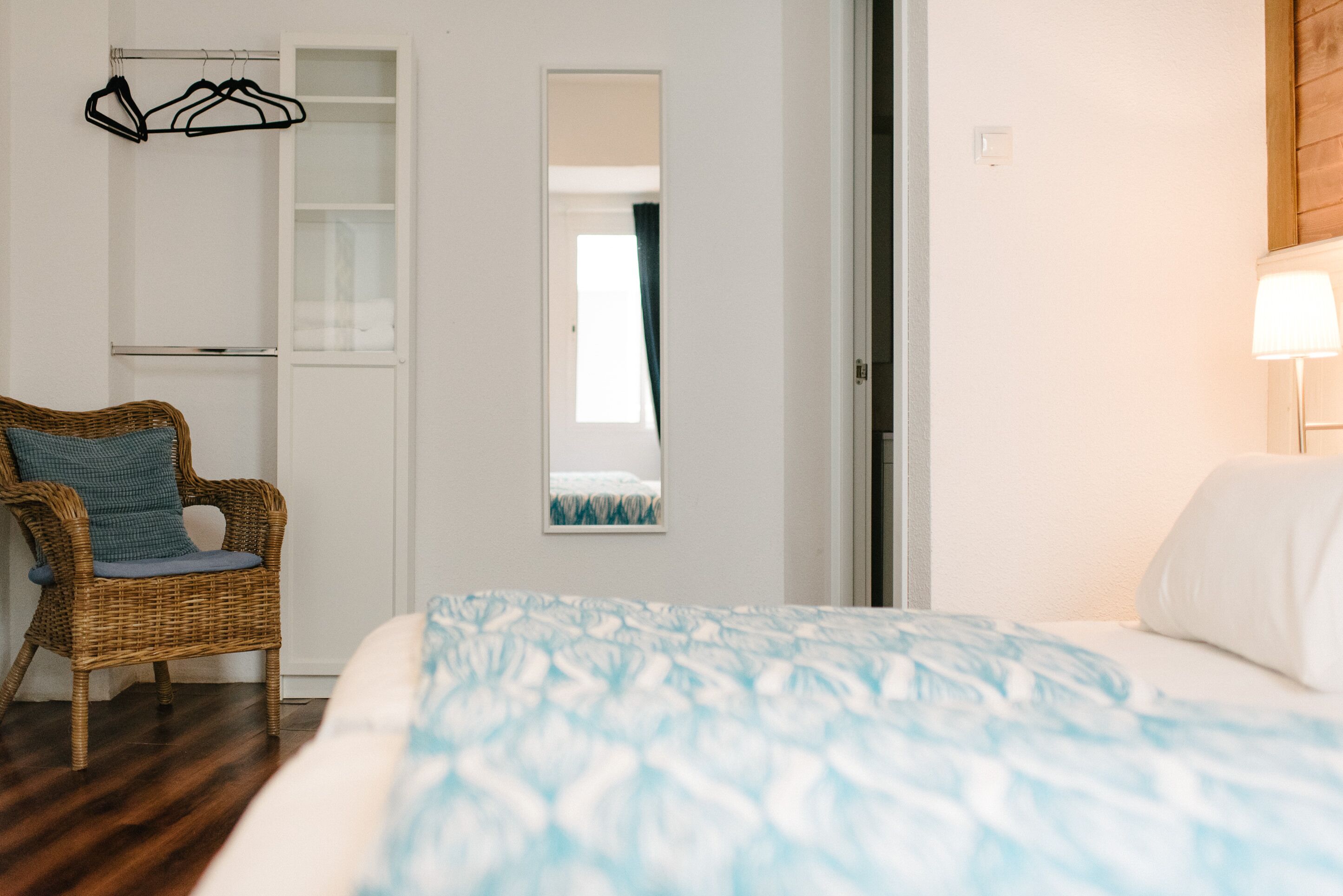 A bedroom with a bed, a wicker chair, a wardrobe, and a mirror.