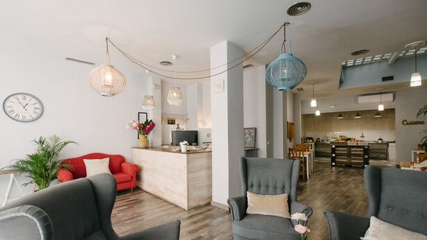 A modern living room with grey sofas, a red sofa, and a kitchen in the background. - The Boutike Guesthouse - Hostel (Seville)