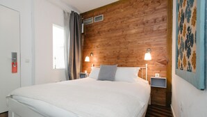 A hotel room with a wooden headboard, two bedside tables with lamps, a large bed with white bedding, and a window with curtains. - The Boutike Guesthouse - Hostel (Seville)