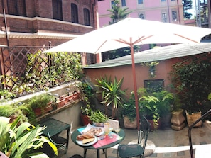 A patio area with a table set for two, surrounded by potted plants and a large umbrella. - Rome Eco Suites (Rome)