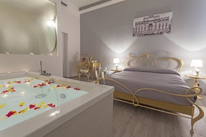 A modern bedroom with a large bathtub filled with rose petals, a bed with a gold frame, and a small bedside table with a lamp. - Rome Eco Suites (Rome)