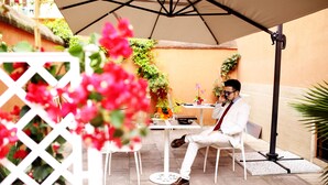 A man sitting at a table under an umbrella, with a white fence and potted plants in the foreground. - Rome Eco Suites (Rome)
