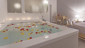A modern bathroom with a large bathtub filled with water and rose petals, a mirror, and a bedside table with a lamp. - Rome Eco Suites (Rome)