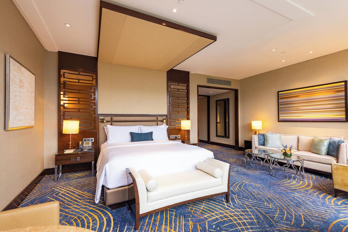 Una habitación de hotel con una cama grande, un sofá, una mesita pequeña y un escritorio con lámpara.