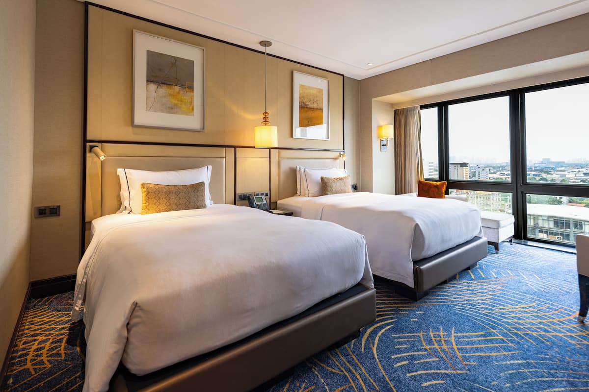 Habitación de hotel con dos camas, un ventanal grande con vista a la ciudad y obras de arte en las paredes.