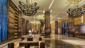 Un hallo espacioso con diseño moderno, que incluye una zona de estar central, amplias columnas decorativas y una pared con motivos a la izquierda.