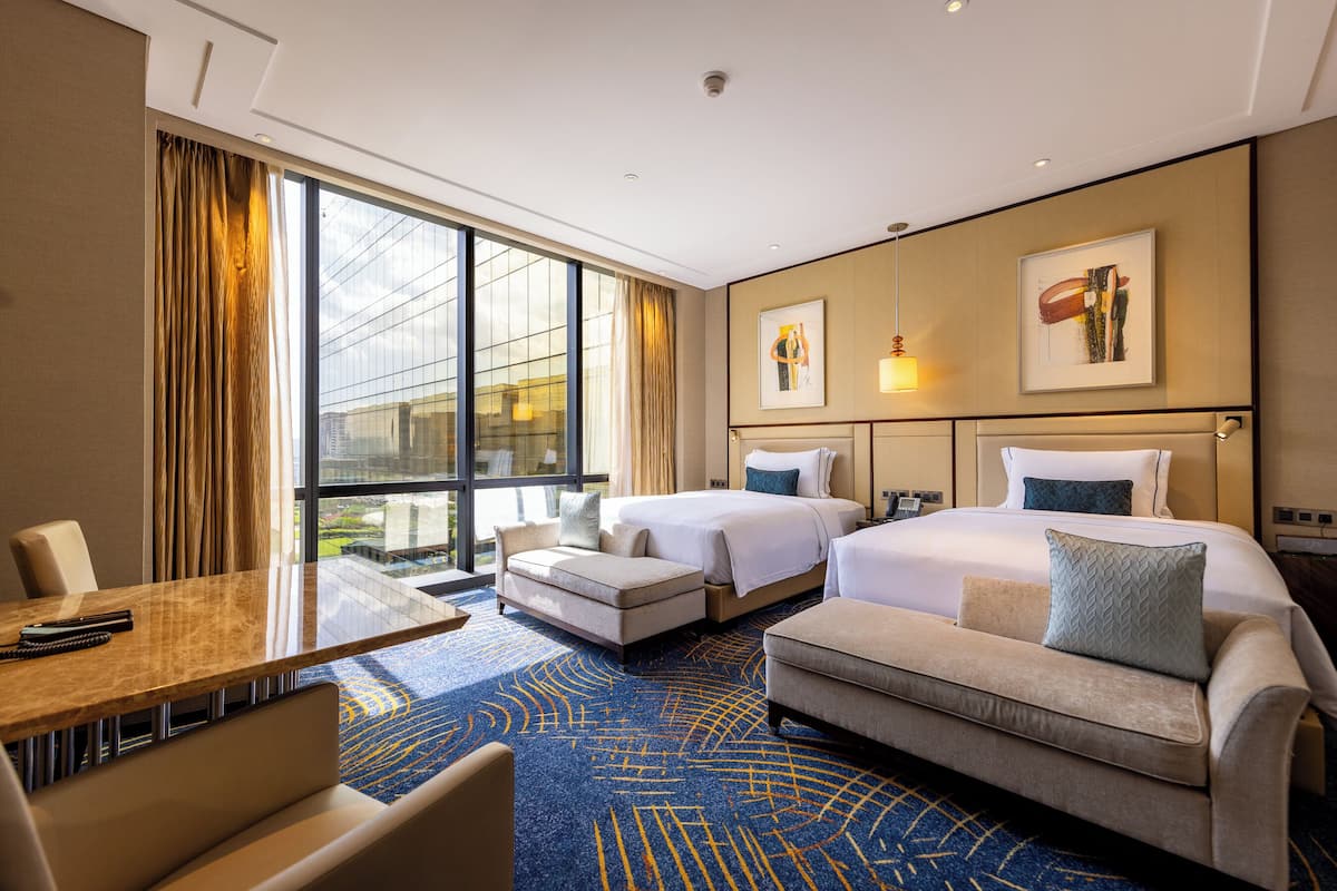 Habitación de hotel con dos camas, un sofá, un escritorio y un ventanal con cortinas.