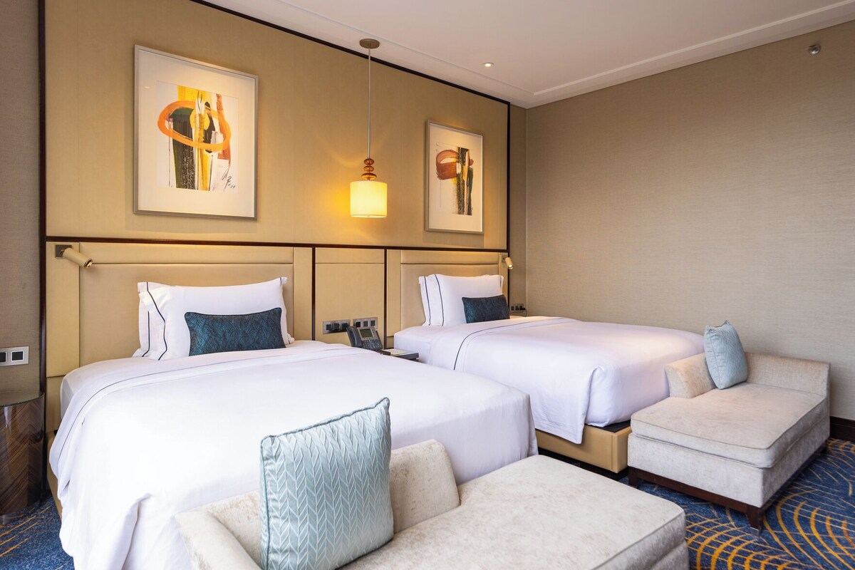 Una habitación de hotel con dos camas, un sofá y obras de arte en las paredes.
