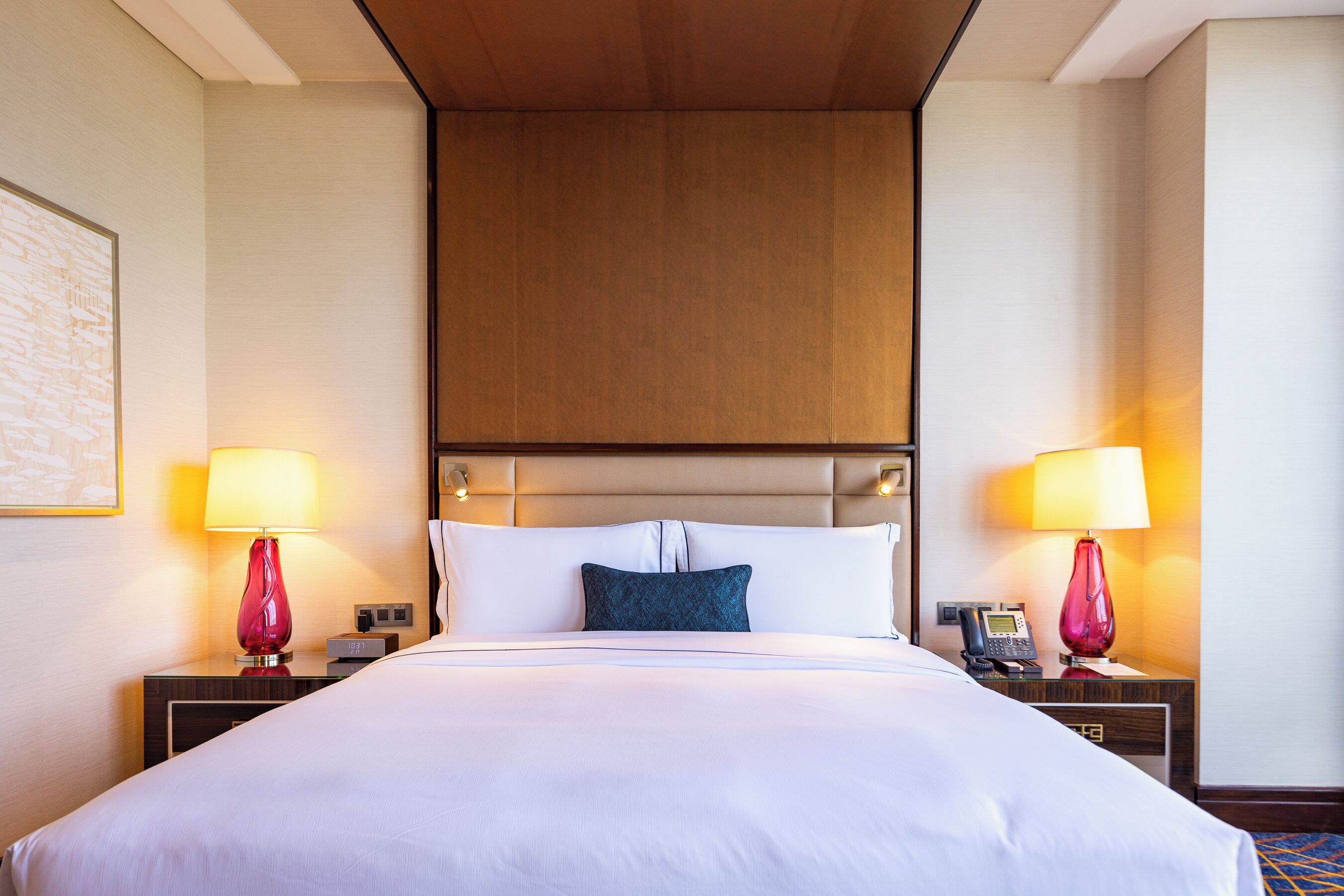 A hotel room with a large bed, two bedside tables with lamps, a headboard, and a framed picture on the wall.