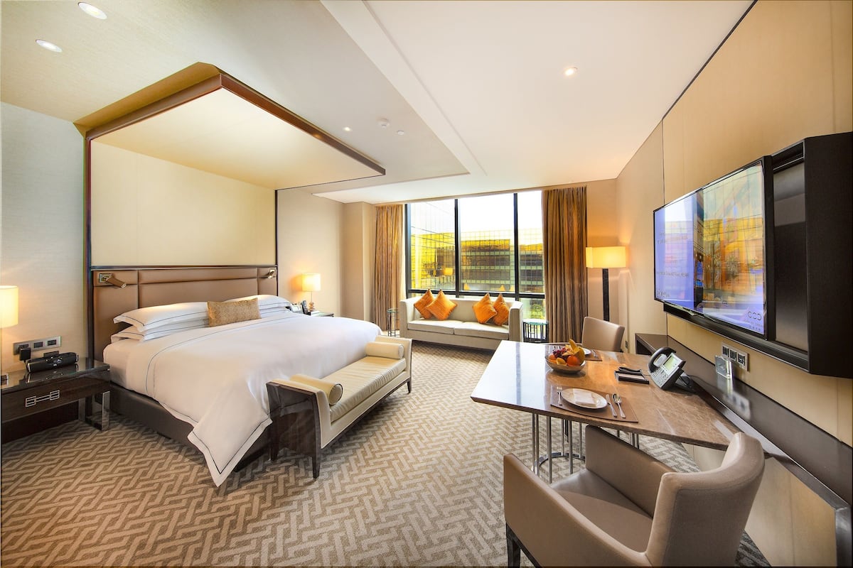 Una habitación de hotel con una cama grande, un escritorio con silla, televisión y ventana con cortinas.